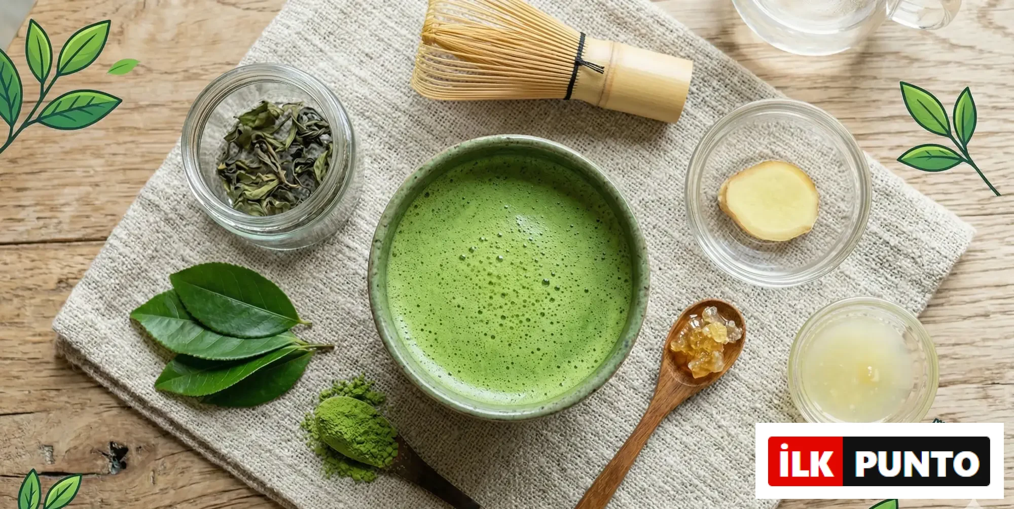 Üstten çekilmiş kompozisyonda seramik kasede köpüklü matcha; yanında bambu çırpıcı, matcha tozu, taze yeşil çay yaprakları, zencefil dilimi ve bal ile doğal keten zemin üzerinde bütünsel bir çay ritüeli.