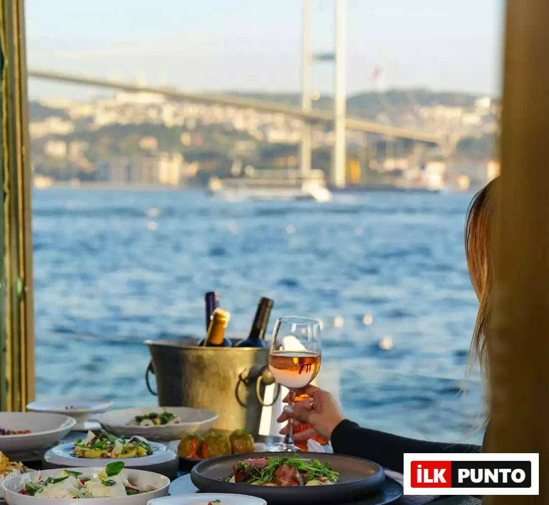 Alp Çekici –: İlk Punto: Alp Çekici – Şeflerin Lezzet Rotaları. Şefin romantik buluşmalar için önerdiği Feriye Restaurant'ta Boğaz'a nazır kurulan şık sofra. Arka planda Boğaziçi Köprüsü manzarası uzanırken, elinde roze şarap kadehi tutan bir kadın özenle sunulan meze ve yemeklerin tadını