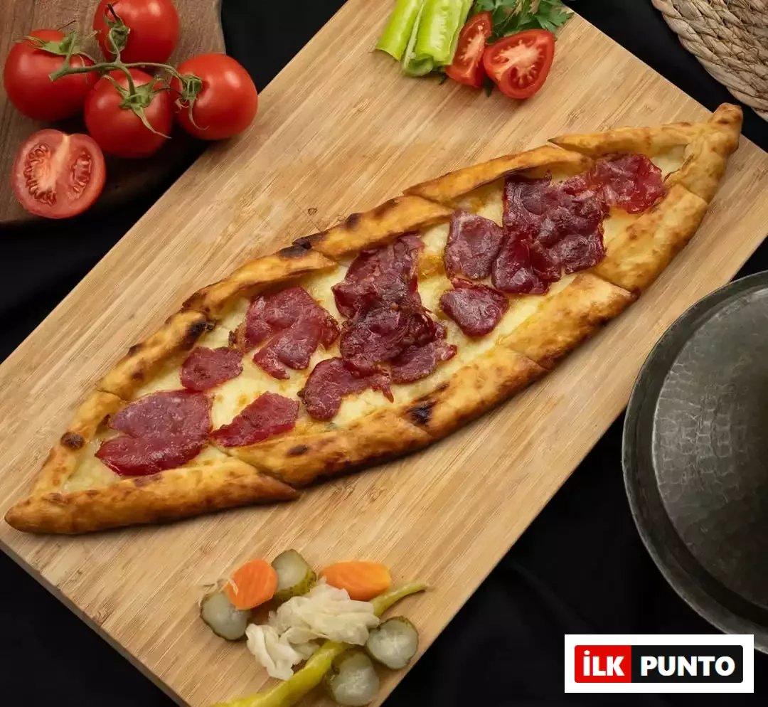 Şefin Pazar kahvaltısı favorisi Pideban Kireçburnu'nu yansıtan pastırmalı ve kaşarlı pide. Ahşap sunum tahtasındaki çıtır pidenin etrafını taze salkım domatesler, yeşil biberler ve iştah açıcı turşular siyah zemin üzerinde zarifçe