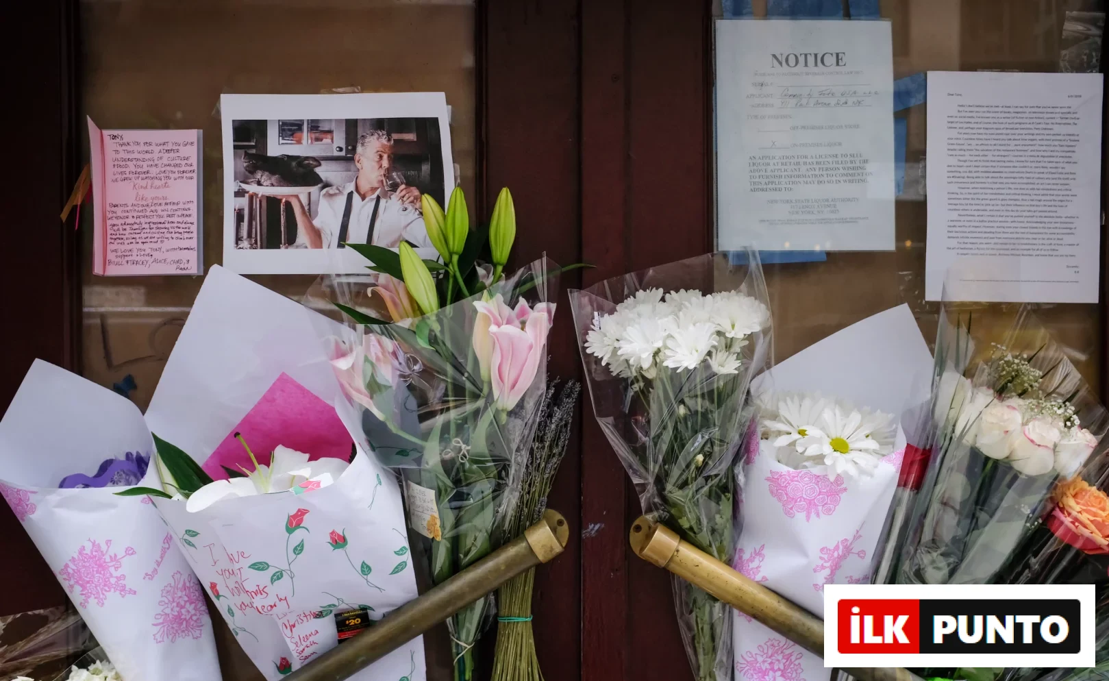 Kapanmış Brasserie Les Halles'in kahverengi kapılarında, Anthony Bourdain'in bir fotoğrafı, üzerinde hayran notları ve beyaz zambak, pembe krizantem ve güllerden oluşan çok sayıda çiçek buketi, onun gastronomi dünyasına yaptığı unutulmaz katkıyı ve modern kaşif ruhunu anmak için toplanmış bir anma yeri görüntüsü sunuyor.