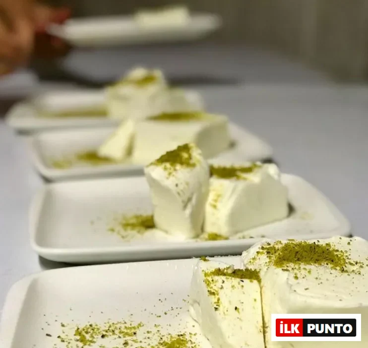 Bir masada sırayla dizili, her birinin üzerinde bolca Antep fıstığı tozu bulunan dikdörtgen beyaz tabaklarda, Maraş dondurmasına özgü kalın kesilmiş, yoğun kıvamlı ve süt beyazı porsiyonlar yer alıyor; en uzakta bir el tabağı masaya bırakırken belirginleşiyor.