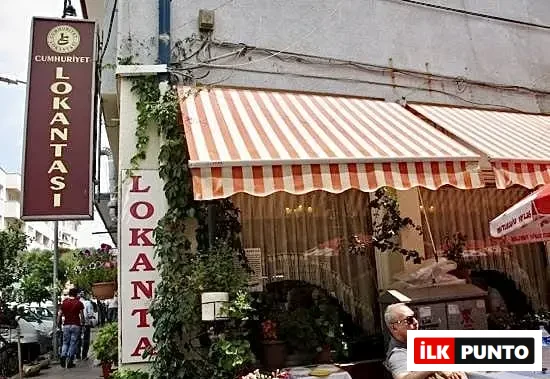 Edremit'in en iyi restoranları arasında yer alan Cumhuriyet Lokantası'nın kırmızı beyaz tentelerle gölgelenen dış cephesi, sarmaşıklarla çevrili sıcak atmosferi ve canlı şehir yaşamını yansıtan görünümü.