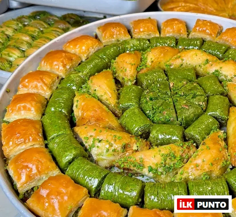Yuvarlak metal tepsiye dairesel düzenle dizilmiş çeşitli şerbetli tatlılar. Dış halkada altın sarısı çıtır kare baklavalar, içe doğru parlak yeşil fıstıklı dürümler, üçgen şöbiyetler ve merkezde yoğun fıstıklı özel kesimler