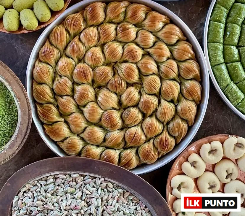 Geleneksel yuvarlak tepside sarmal düzende dizilmiş çıtır midye baklavalar; etrafını saran taze iç fıstık dolu bakır kâseler, fıstıklı dürümler ve kurabiyeler eşliğinde Türk mutfağının köklü tatlı zanaatını kusursuzca sergiliyor.