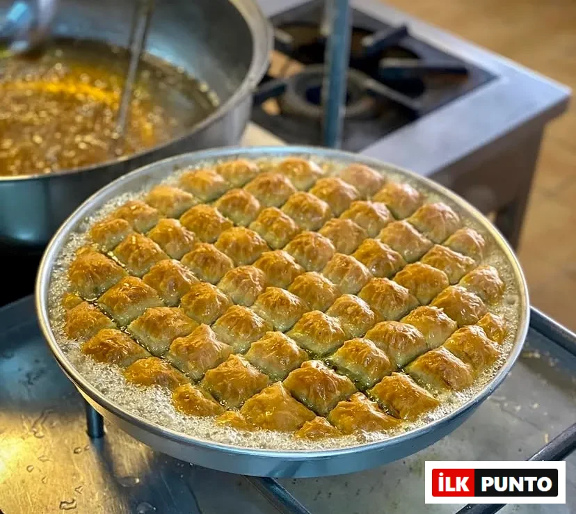 Türkiye’nin: İlk Punto Türkiye'nin En İyi Baklavacıları: Profesyonel mutfak ocağında, yuvarlak metal tepsi içindeki taze pişmiş altın sarısı baklava dilimleri üzerinde köpüren sıcak şerbet. Arka plandaki kaynayan şerbet tenceresiyle, ustalık gerektiren geleneksel tatlı yapım aşaması