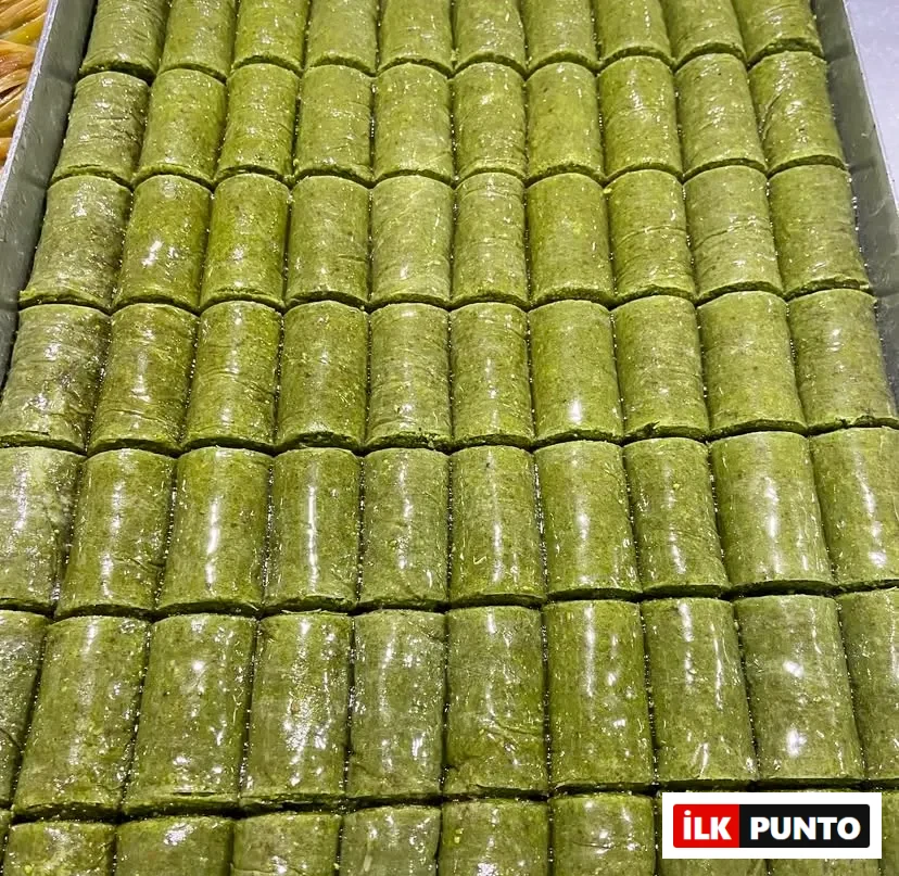 Metal tepsiye nizami sıralanmış, şerbetiyle parlayan yemyeşil fıstıklı dürüm baklavalar. İncecik yufkayla sarılan yoğun Antep fıstıklı bu ikonik tat, geleneksel Türk tatlı kültürünün benzersiz ustalığını ve görsel