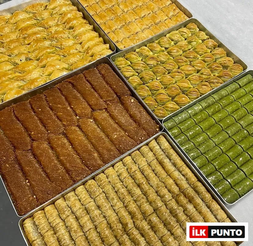 Altın sarısı ve fıstık yeşili tonlarındaki çıtır geleneksel tatlılar metal tepsilerde sergileniyor. Yan yana dizilmiş fıstıklı dürüm, midye baklava, şöbiyet ve burma kadayıf çeşitleri, Türk mutfağının eşsiz lezzet zenginliğini
