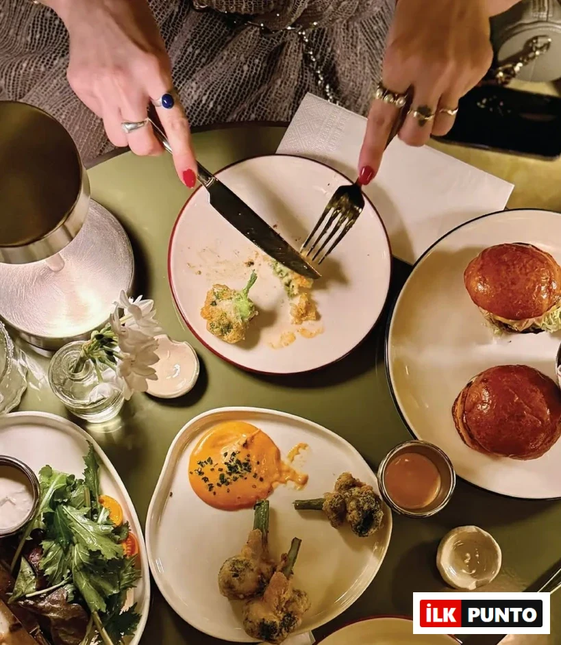 Kiff Bebek restoranında çekilen bu üstten görünüm fotoğrafında, kırmızı ojeli ve yüzüklü ellerin yeşil bir masada, kızarmış brokoli tempurayı bıçak ve çatalla kestiği an net bir şekilde görülüyor; masada ayrıca salata, soslu brokoli ve bürgerler gibi çeşitli özel lezzetler iştah açıcı bir şekilde sergileniyor.
