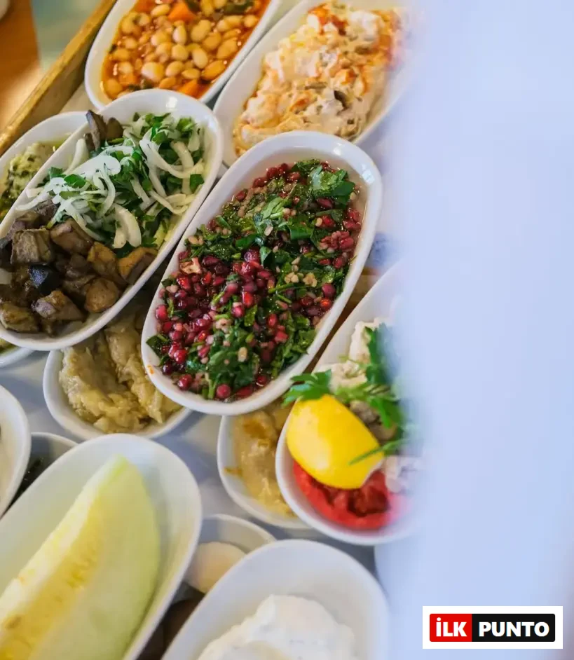 İsmet Baba restoranında sunulan zengin meze çeşitlerinden oluşan masa üst görünümü; beyaz oval tabaklarda barbunya pilaki, közlenmiş patlıcanlı salata, nar taneli yeşil salata, limon ve közlenmiş kırmızı biber, bir dilim kavun ve haydari gibi geleneksel lezzetlerin iştah açıcı sunumu.