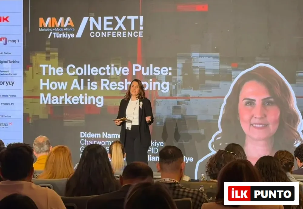MMA NEXT! Konferansı'nda sahnedeki Didem Namver, büyük bir ekranda Yapay Zeka'nın Pazarlama'yı nasıl yeniden şekillendirdiğini gösteren sunumu yaparken izleyicilere dönük konuşuyor ve ekranda kendisinin gülümseyen bir portresi de görülüyor.