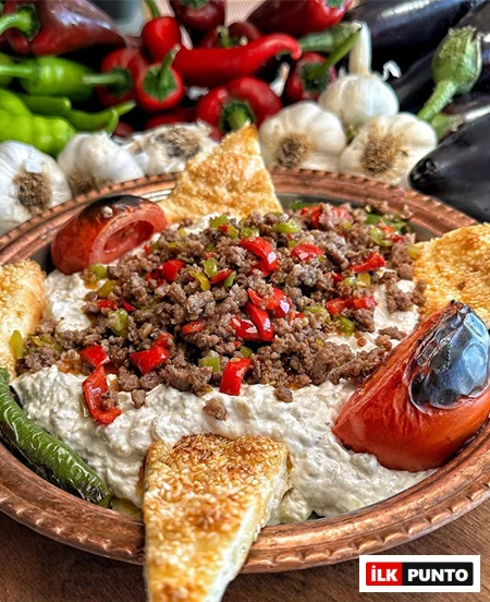 Bakır tepside servis edilen, közlenmiş patlıcan ezmesi üzerinde renkli biberlerle harmanlanmış kıymalı harcın, közlenmiş domates ve biberlerin ve susamlı pide üçgenlerinin bir araya geldiği bu eşsiz sunum, Antalya'nın en iyi restoranlarında tadabileceğiniz zengin Türk mutfağı lezzetlerini yansıtıyor.