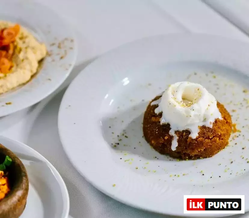 Antalya'da sunulan zengin Akdeniz mutfağının bir parçası olarak, üzeri dondurmalı veya kaymaklı, çevresi yeşil fıstık ve baharat serpilmiş yuvarlak irmik helvası, odak dışındaki çeşitli mezelerle birlikte keyifli bir gastronomi deneyimini yansıtmaktadır.