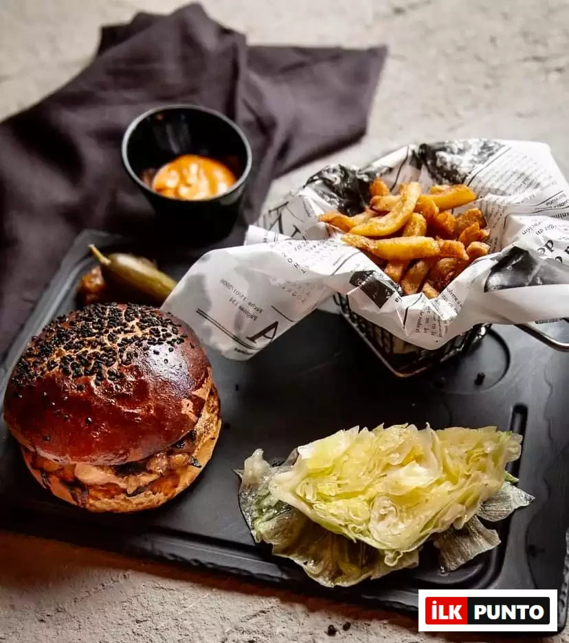 Antalya'nın en beğenilen hamburger restoranlarından birinde şık bir sunumla servis edilen, siyah susamlı hamburger ekmeği, çıtır patates kızartması, özel sosu ve yanında taze göbek marul ile turşusuyla iştah açıcı bir hamburger tabağı.