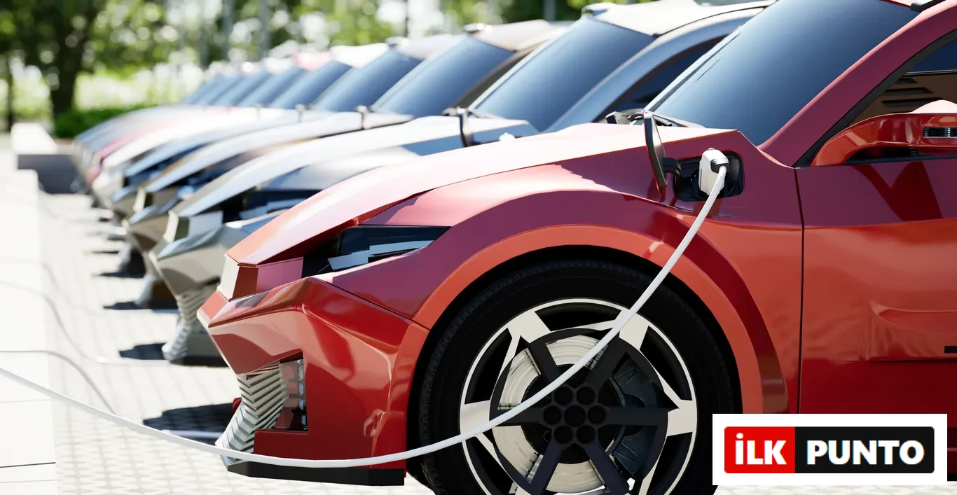 Kırmızı, modern tasarımlı bir elektrikli araç, şarj istasyonunda beyaz bir kabloyla şarj olurken, arkasında enerji dönüşümünün ve elektrifikasyonun simgesi olan benzer birçok elektrikli araç sırayla park etmiş durumda, gümüşün bu elektrikli araçlar ve enerji dönüşümü bağlamındaki artan stratejik önemini vurguluyor.