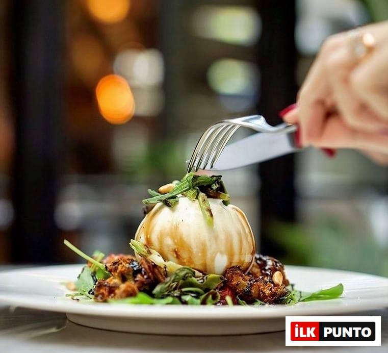 Etiler ve Akatlar'ın öne çıkan lezzet duraklarından birinde, balzamik sos gezdirilmiş, roka ve çam fıstıklarıyla zenginleştirilmiş nefis bir burrata peyniri tabağı, bir elin çatal bıçakla kesmeye hazırlandığı iştah açıcı bir sunumla dikkat çekiyor.