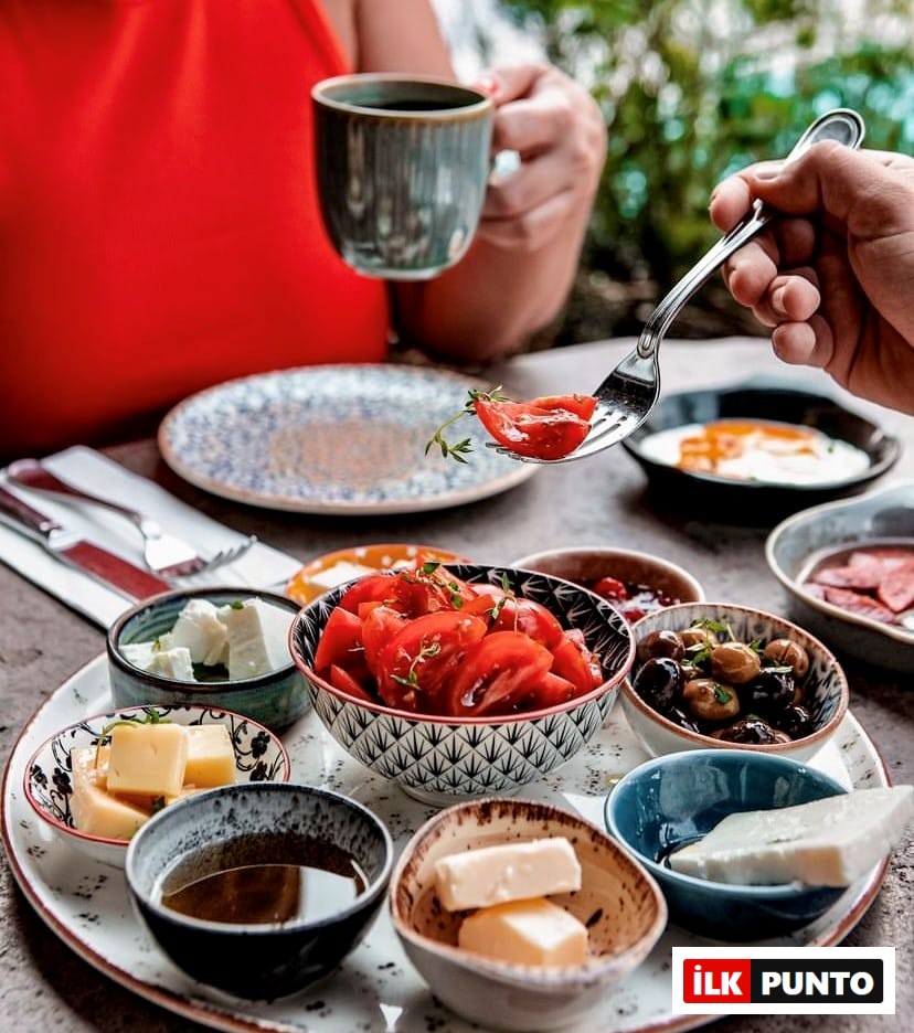 Etiler ve Akatlar'ın seçkin mekanlarından Minoa Village'da, yemyeşil bir bahçe ortamında kahvaltı keyfi yapan iki kişiden biri kahvesini içerken, diğeri zengin kahvaltı tabağındaki taze doğranmış domates, peynir, zeytin ve balla dolu küçük kaselerin arasından çatalıyla bir dilim domates alıyor.