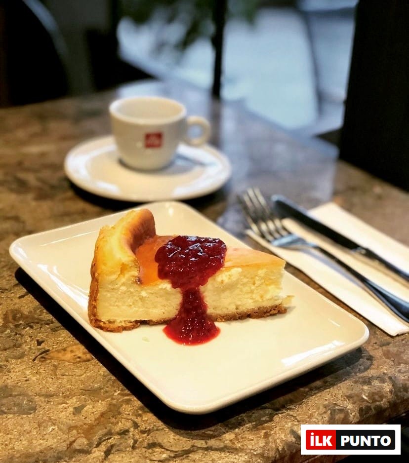 Mermer yüzeyli bir masada, üzerinde parlak kırmızı, akışkan meyve sosuyla zenginleştirilmiş, fırınlanmış, kremamsı dokuya sahip cazip bir dilim cheesecake, küçük bir kahve fincanı ve çatal bıçak takımı eşliğinde sunularak, Etiler ve Akatlar'daki gurme lezzet duraklarının vazgeçilmez tatlı seçeneklerinden birini gözler önüne seriyor.