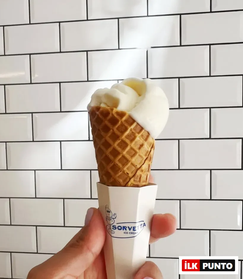 Beyaz metro fayansları önünde, açık renk ojeli bir el, üzerinde Sorvetta logosu bulunan özel karton tutacaklı, hafifçe eriyerek waffle külahından taşan bol ve kremsi vanilyalı dondurmayı serinletici bir lezzet olarak sunuyor.