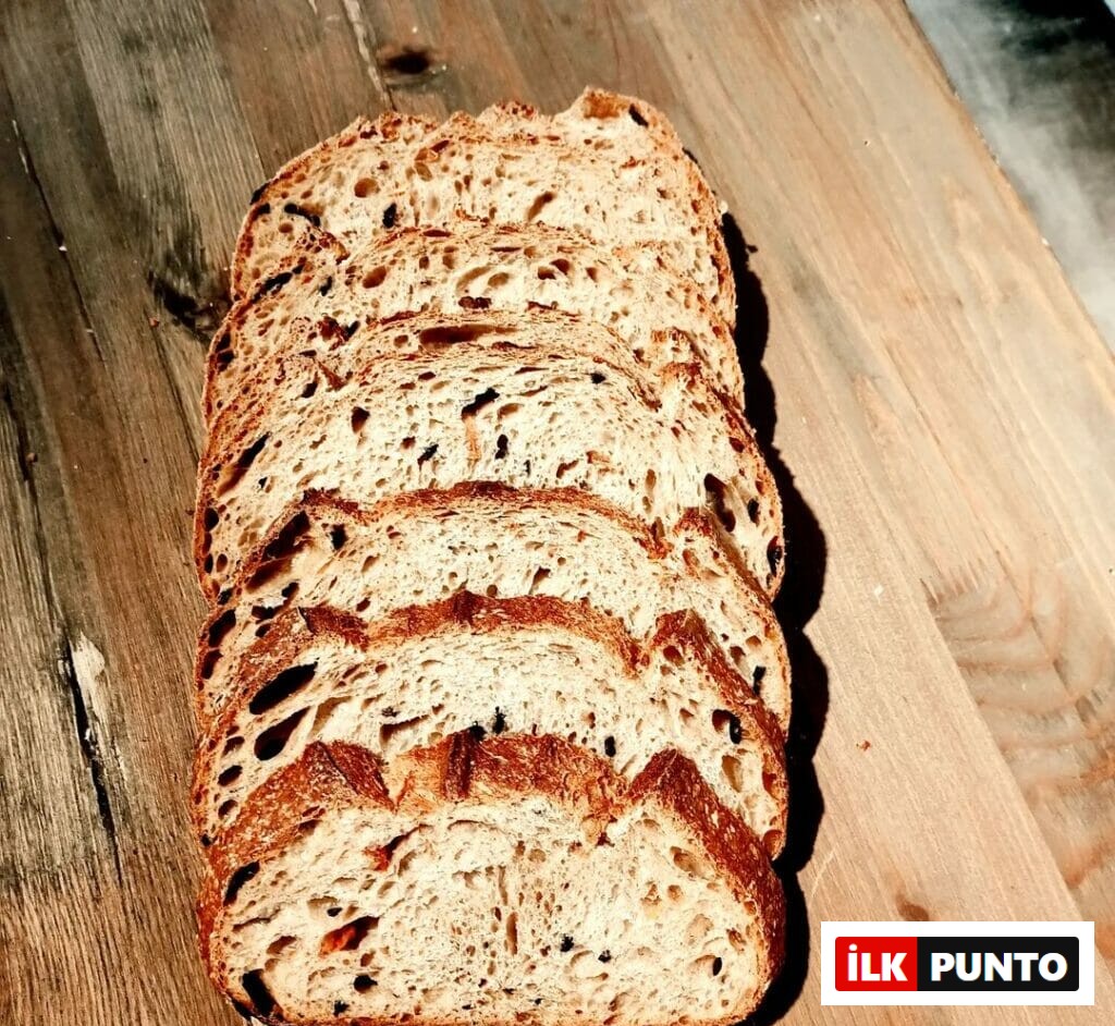 Breadtaking’in el yapımı ekşi mayalı zeytinli ekmeği; ahşap zemin üzerinde dilimlenmiş halde sunulmuş.