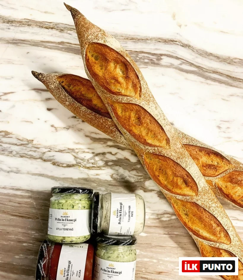 Pelin’in Ekmeği’ne ait çıtır baget ekmekler; yanında acuka, otlu tereyağı, tulum peyniri pate ve Girit ezmesi kavanozlarıyla mermer tezgâh üzerinde sunuluyor.