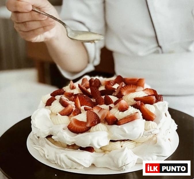 Bir şefin beyaz kremalı ve bol taze çilek dilimleriyle zenginleştirilmiş büyük bir beze pastasına ustalıkla sos gezdirdiği bu iştah açıcı görüntü, İstanbul'un huzurlu bahçeli mekanlarında deneyimlenebilecek özel tatlı seçeneklerinden birini gözler önüne seriyor.