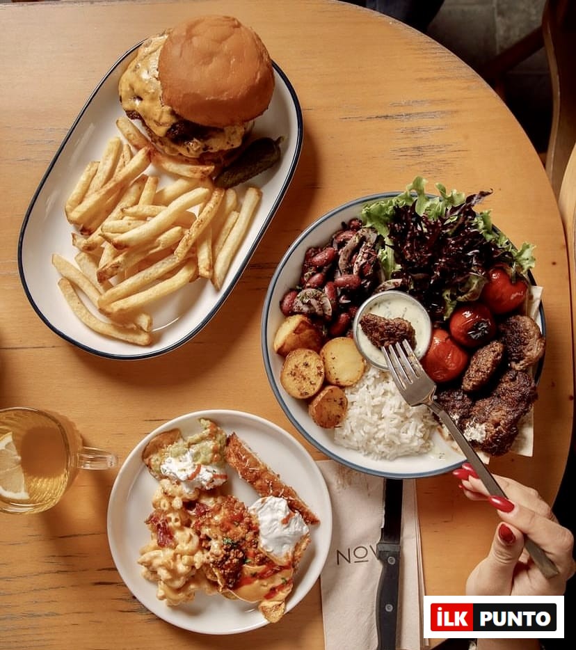 İstanbul'un keyifli bahçeli mekanlarından Nove Garden'da, peynirli burger ve patates kızartması, bol malzemeli bir kase yemek ve kremalı makarnadan oluşan zengin menüden lezzetli seçenekler sunan dolu bir masa.