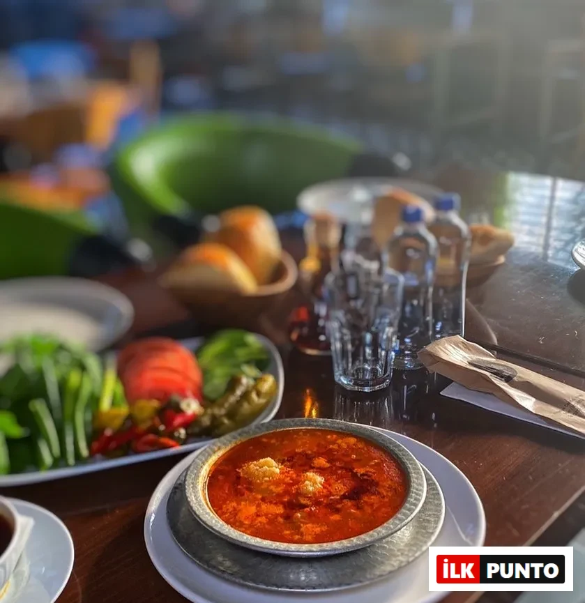 Etiler Sarıhan Gusto’da servis edilen kırmızı renkli kelle paça çorbası, yanında yeşillikler ve turşularla birlikte.