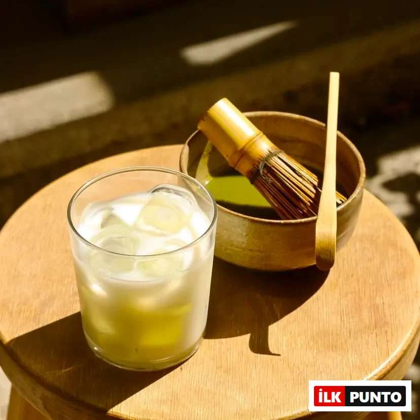 Poco Matcha'da ahşap bir tabure üzerinde buzlu bir matcha içeceği ve yanında matcha hazırlamakta kullanılan bambu kaşık ve çırpıcı gibi gereçlerin bulunduğu bir kase.