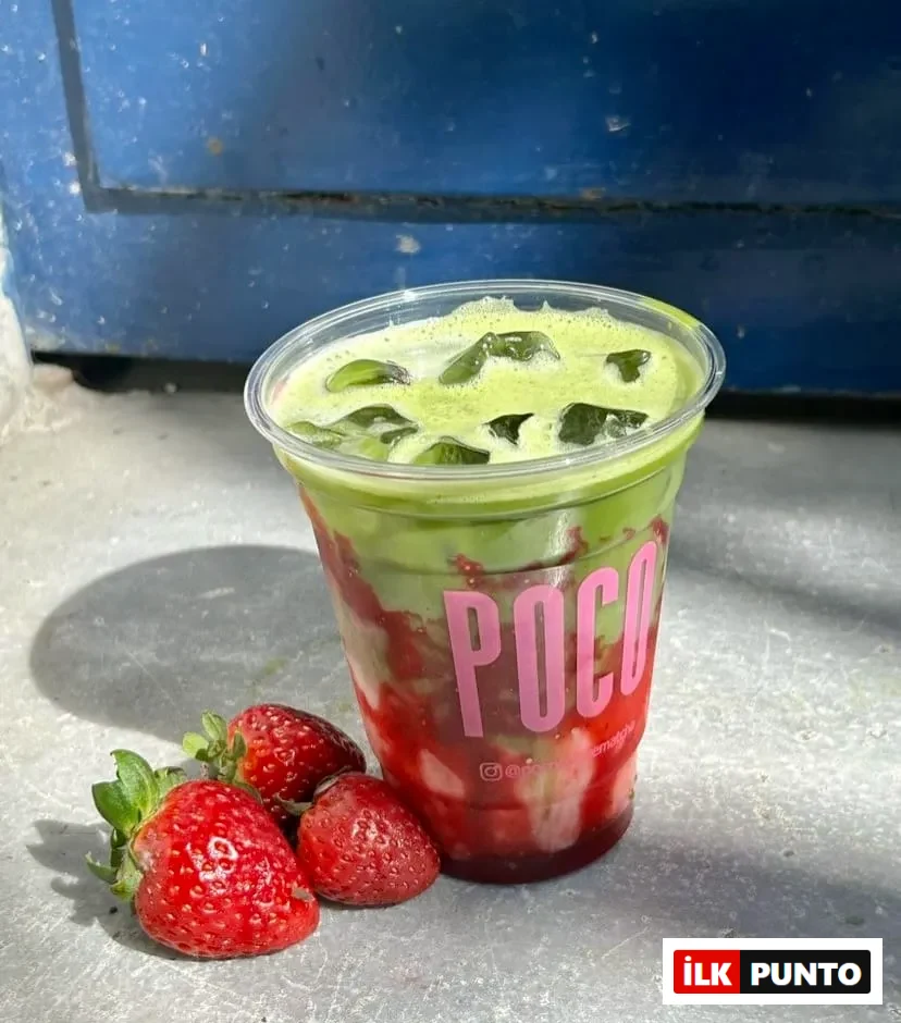 Poco Matcha'da sunulan, buzlu ve çilek soslu matcha içeceğinin yakın çekim fotoğrafı. İçecek, Poco logosunun bulunduğu şeffaf bir bardakta servis ediliyor ve yanında üç adet taze çilek bulunuyor.