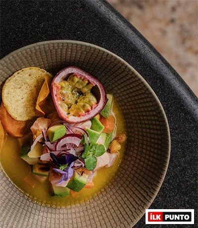 Suadiye'deki Machi'de servis edilen, bir kasede avokado, kırmızı soğan, balık ve passiflora meyvesi ile süslenmiş bir ceviche tabağının yakın çekimi. Yanında tortilla cipsleri de duruyor.