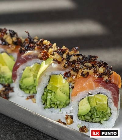 Ken Sushi & More'da masada servis edilen, üzerinde somon füme, avokado ve kurutulmuş domates bulunan, farklı soslarla zenginleştirilmiş özel bir sushi tabağı