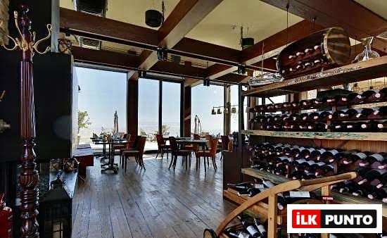Kapadokya'nın eşsiz manzarasını içeri taşıyan geniş pencereleri, ahşap zeminleri ve tavan kirişleriyle sıcak bir atmosfere sahip bu şık yemek mekanında, çeşitli şarap şişeleriyle dolu büyük raflar ve zarifçe düzenlenmiş masalar, misafirlerini bekliyor.