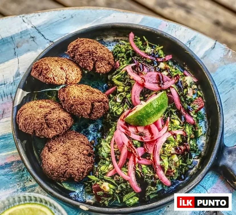Kaş'taki Pells restoranında servis edilen bu tabakta, beş adet altın rengi çıtır falafel köftesi, taze yeşil otlar ve ince kıyılmış sebzelerden oluşan salata, üzerine parlak pembe soğan turşusu, koyu renkli bir sos ve bir dilim misket limonu eklenerek sunulan zengin ve lezzetli bir öğün görülmektedir.