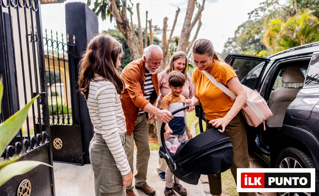 Aile üyeleri (büyükbaba, büyükanne, anne, baba ve iki çocuk), gülümseyerek arabadan bebek oto koltuğunu indirirken, bu an aile seyahati için yapılan tatlı hazırlıkları gözler önüne seriyor.