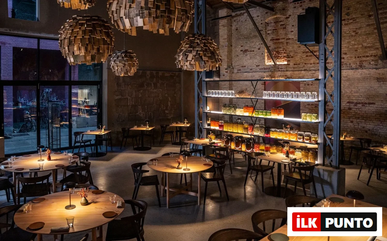 Esse Restaurant'ın geniş iç mekanında, ahşap parçalı şık avizelerin loş ışıklarla aydınlattığı modern ve endüstriyel bir tasarımla döşenmiş, boş ahşap masalar sıralanıyor, duvarlardaki tuğla dokusu ve renkli kavanozların sergilendiği raflar mekana sıcak bir ambiyans ve özel bir yemek deneyimi katıyor.