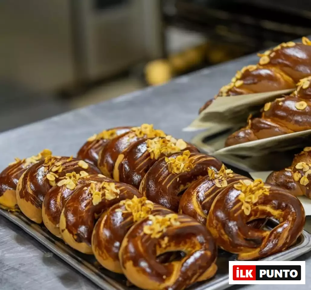 İlk Punto'nun Salvatore Cannetiello – Şeflerin Lezzet Rotaları yazısında şefin favori duraklarından İnci Pastanesi'ni temsil eden görselde, metal tepsi üzerinde taze pişmiş, parlak dokulu ve file badem süslemeli geleneksel ay çörekleri iştah açıcı bir şekilde sergileniyor.