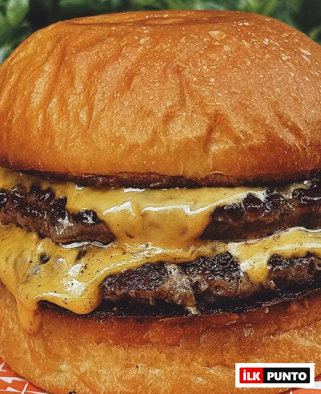 İlk Punto Salvatore Cannetiello – Şeflerin Lezzet Rotaları içeriğinde şefin favori mekanı Zula'yı temsil eden çift köfteli cheeseburger. Parlak brioche ekmeği arasında, kenarlarından erimiş peynir süzülen iki kalın köfte, turuncu beyaz desenli sarma kağıdı üzerinde iştah açıcı duruyor.