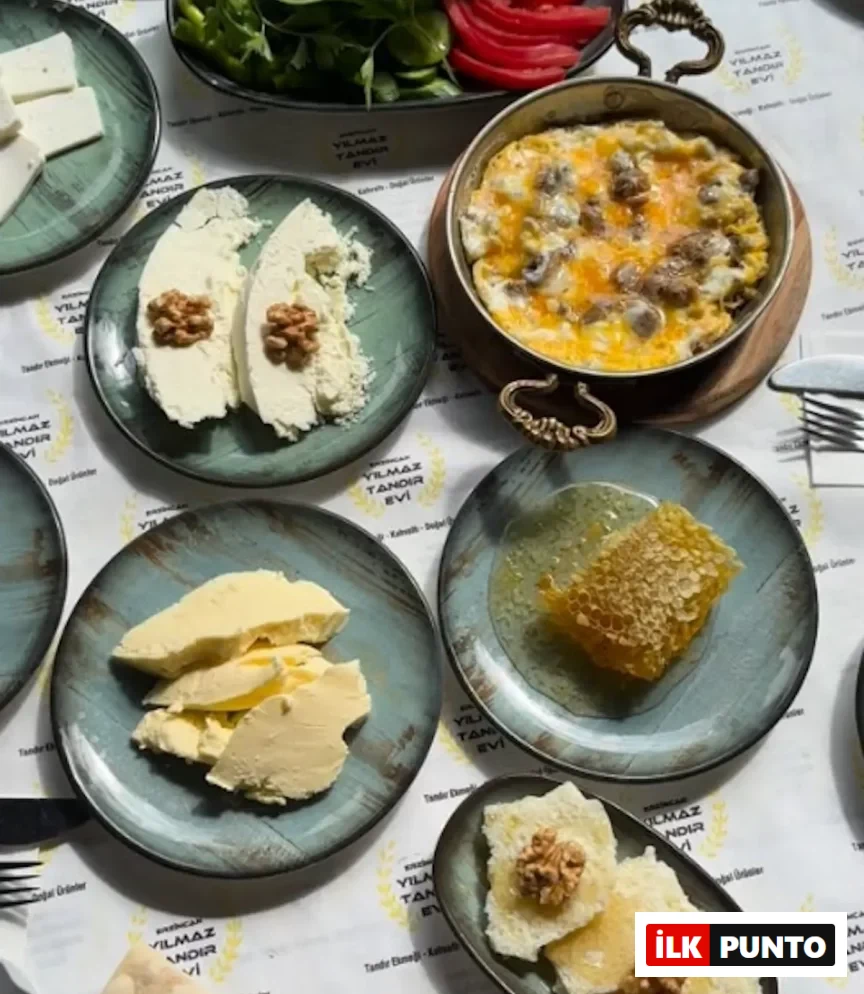 Erzincan'daki en iyi kahvaltı deneyimlerinden birini sunan Yılmaz Tandır Evi'nde, masayı dolduran petek balı, dilimlenmiş doğal tereyağı, demir tavada servis edilen kavurmalı yumurta, cevizli tulum peyniri, beyaz peynir ve ballı cevizli ekmek dilimleri gibi yöresel lezzetlerin bir araya geldiği zengin ve iştah açıcı bir Türk kahvaltısı sofrası.