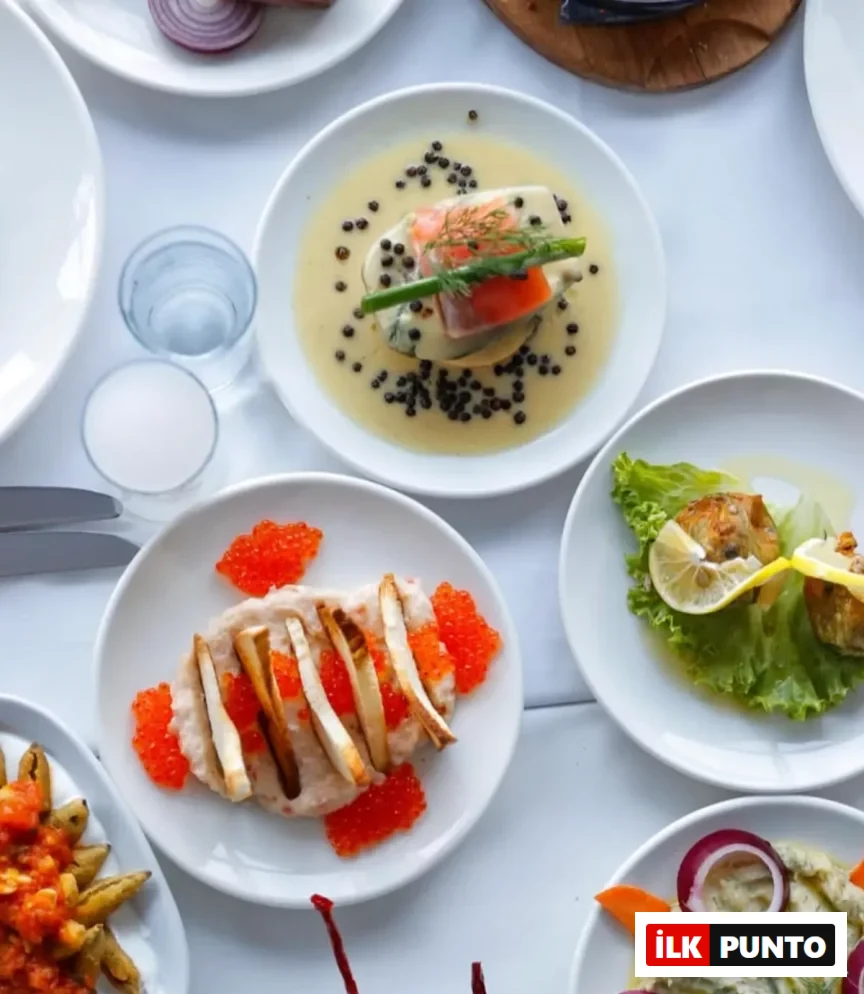 Arnavutköy'deki bir balık restoranında beyaz bir masanın üzerinde sunulan, kremalı somon, parlak kırmızı havyarla süslenmiş fava, limon dilimli kızarmış balık ve mor soğanlı mezeler gibi özenle hazırlanmış çeşitli deniz ürünleri ve meze tabakları.