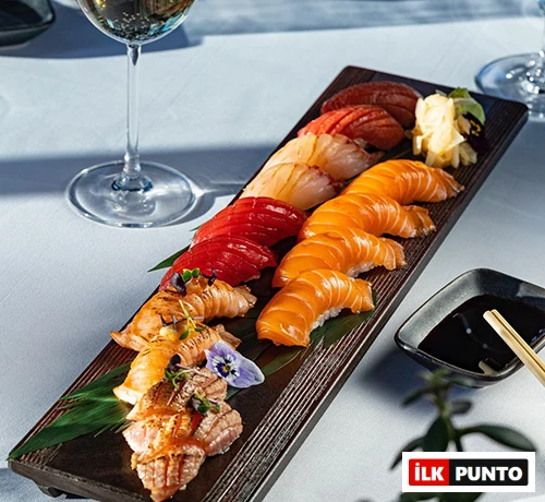 Narince hazırlanmış somon, orkinos ve közlenmiş balık nigiri çeşitlerinin yenilebilir çiçeklerle süslenerek sunulduğu uzun, koyu renk ahşap bir servis tabağı, İstanbul’un en popüler sushi restoranlarından birindeki zarif bir lezzet şölenini gözler önüne seriyor.