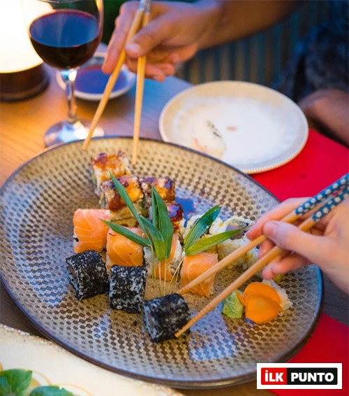 Birbirinden farklı somonlu, koyu renkli ve soslu çeşitleriyle özenle hazırlanmış bir tabak dolusu sushinin önünde, iki kişinin çubuklarla keyifle sushi seçtiği bu detaylı görüntü, İstanbul’un en iyi sushi restoranlarındaki zengin Uzak Doğu mutfağı deneyimini yansıtıyor.
