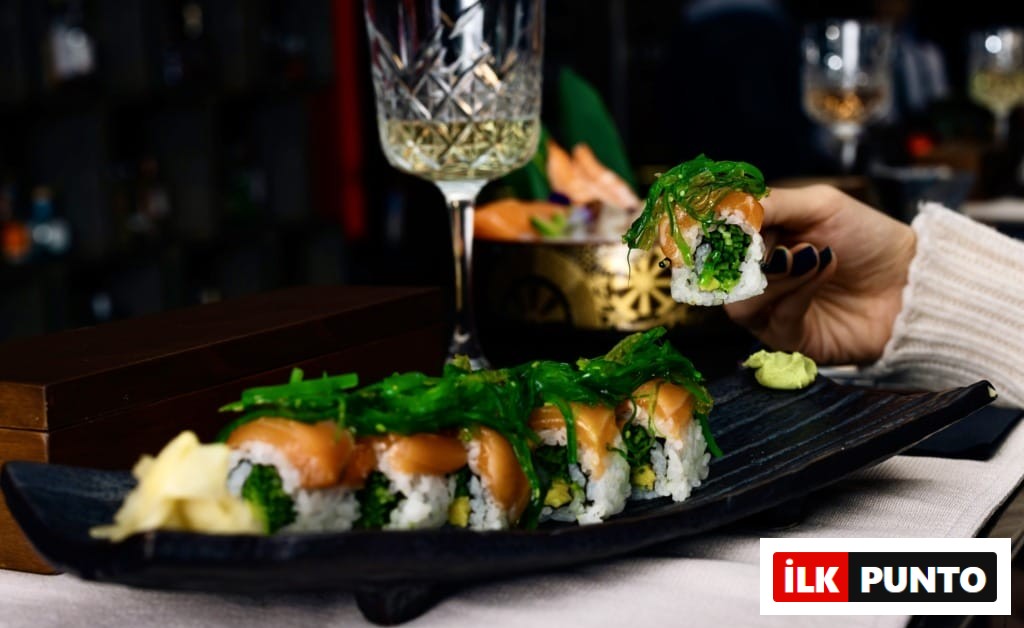 Bir elin zarifçe chopsticklerle kaldırdığı, üzerinde taze somon ve parlak yeşil wakame yosunu bulunan, şık siyah bir tabakta özenle dizilmiş maki sushi ruloları, İstanbul’un popüler sushi restoranlarından birindeki rafine Uzak Doğu lezzetlerini ve kaliteli sunumu vurguluyor.