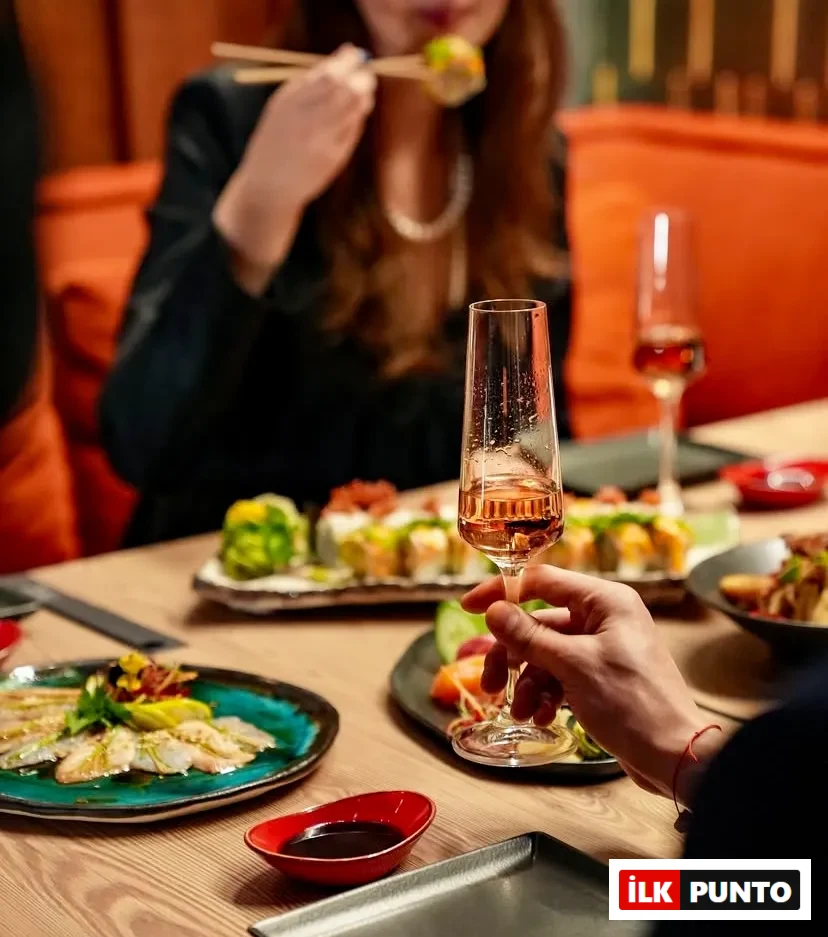 Bir kadın İstanbul'un popüler sushi restoranlarından biri olan Sushi Manga'da masadaki çeşitli taze ve özenle hazırlanmış sushi roll'larından, levrek carpaccio'sundan ve özel soslardan tadarken, yakındaki bir el şık bir kadehte pembe şarabı tutarak bu modern Uzak Doğu deneyiminin keyfini çıkarıyor.