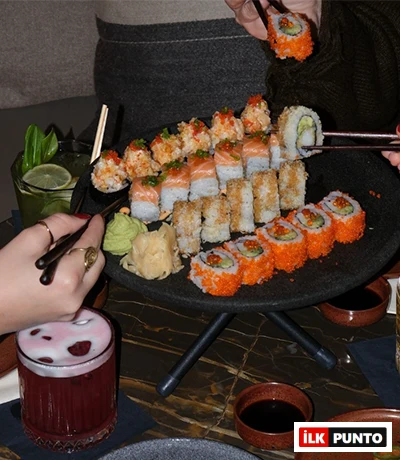 İstanbul'un önde gelen modern sushi duraklarından birinde, üzerinde turuncu tobiko kaplı, somonlu ve yengeçli gibi çeşitli sushi roll'larının sunulduğu siyah katlı servis tabağı etrafında, taze wasabi ve zencefil eşliğinde keyifli bir Uzak Doğu lezzet deneyimi paylaşılıyor.