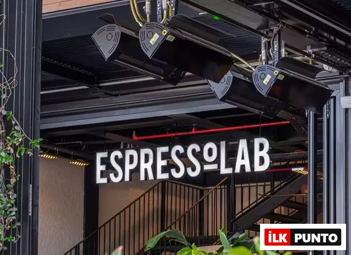 İlk Punto - Terminal Kadıköy Rehberi: Lezzet, Alışveriş ve Eğlence Durakları. Terminal'in kahve noktası Espressolab'in endüstriyel tasarımı. Siyah metal merdivenler ve ısıtıcılar altında asılı parlak beyaz tabela, yeşil yapraklar arasından ziyaretçileri kahve molasına davet ediyor.