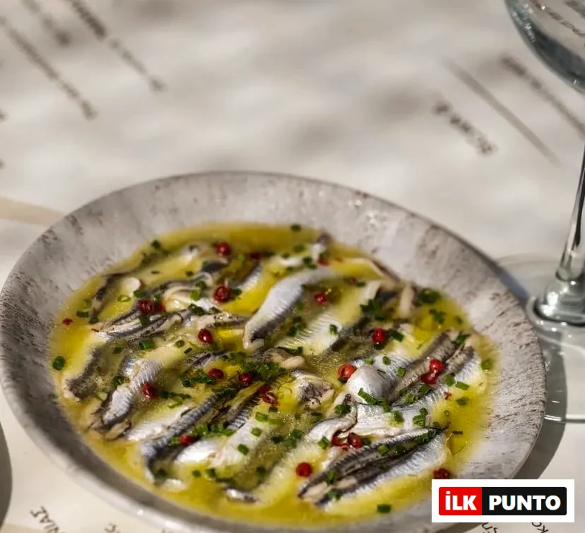 Gri ve dokulu oval bir tabakta, Selanik'in meşhur Mamalouka restoranında sunulan, zeytinyağlı marinasyon içinde bekletilmiş, üstüne ince doğranmış taze soğan ve pembe tane karabiber serpilmiş parlak gümüş renkli marine ançuezler, yazıların okunabildiği beyaz bir masa üzerinde iştah açıcı bir meze olarak yer alıyor.
