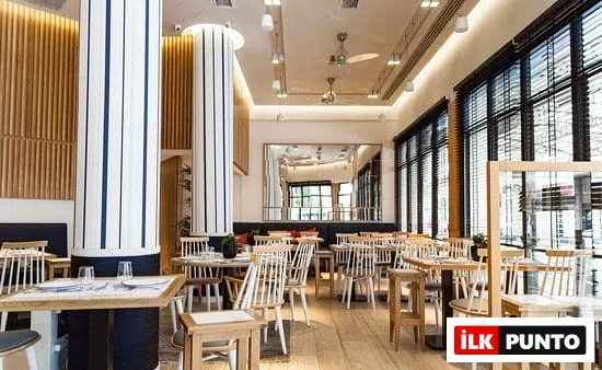 Selanik'in zarif ve sıcak ambiyansıyla öne çıkan deniz ürünleri restoranlarından birinin içi; beyaz-koyu mavi çizgili sütunlar, ahşap çıtalı duvarlar ve çok sayıda boş masa düzeniyle aydınlık, modern bir yemek alanı sunuyor.