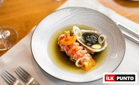 Bir Selanik restoranında özenle sunulan bu fotoğraf, parlak kırmızı ıstakoz veya kerevit kuyruğu, siyah havyarla süslenmiş taze bir istiridye ve berrak, aromatik sosuyla beyaz bir tabakta zarifçe düzenlenmiş, şehrin gastronomi kalitesini yansıtan nefis bir deniz ürünü tabağını gözler önüne seriyor.