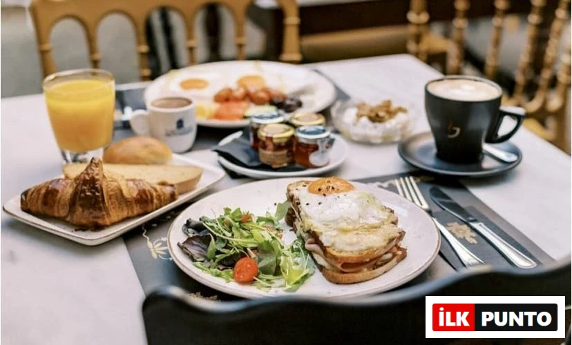 Selanik'teki Koukos'ta, sahanda yumurta ile servis edilen Croque Madame'ın yanında taze yeşil salata, kruvasan, ekmek çeşitleri, portakal suyu, kahve, farklı reçeller ve yoğurtlu kuruyemişler içeren zengin bir kahvaltı masası, zarif bir atmosferde iştah açıcı bir görüntü sunuyor.