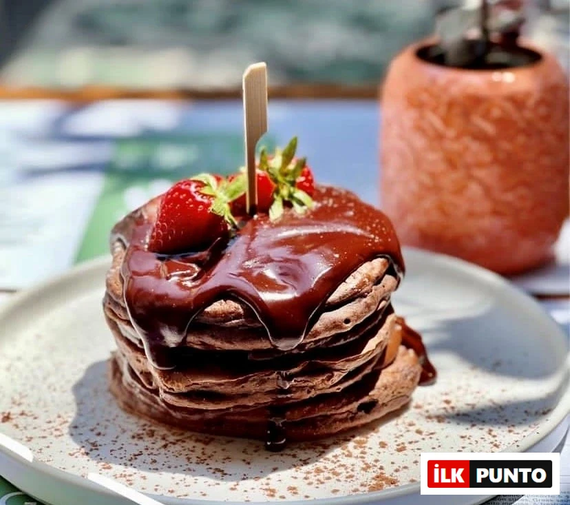 Selanik'in popüler kahvaltı mekanlarından Garden Bar'da sunulan, üzeri bol akışkan çikolata sosu ve kırmızı taze çileklerle süslenmiş, kakao serpilmiş beyaz tabakta duran yumuşacık ve iştah açıcı çikolatalı pankek yığını, şehrin en iyi kahvaltı seçeneklerinden birini gözler önüne seriyor.